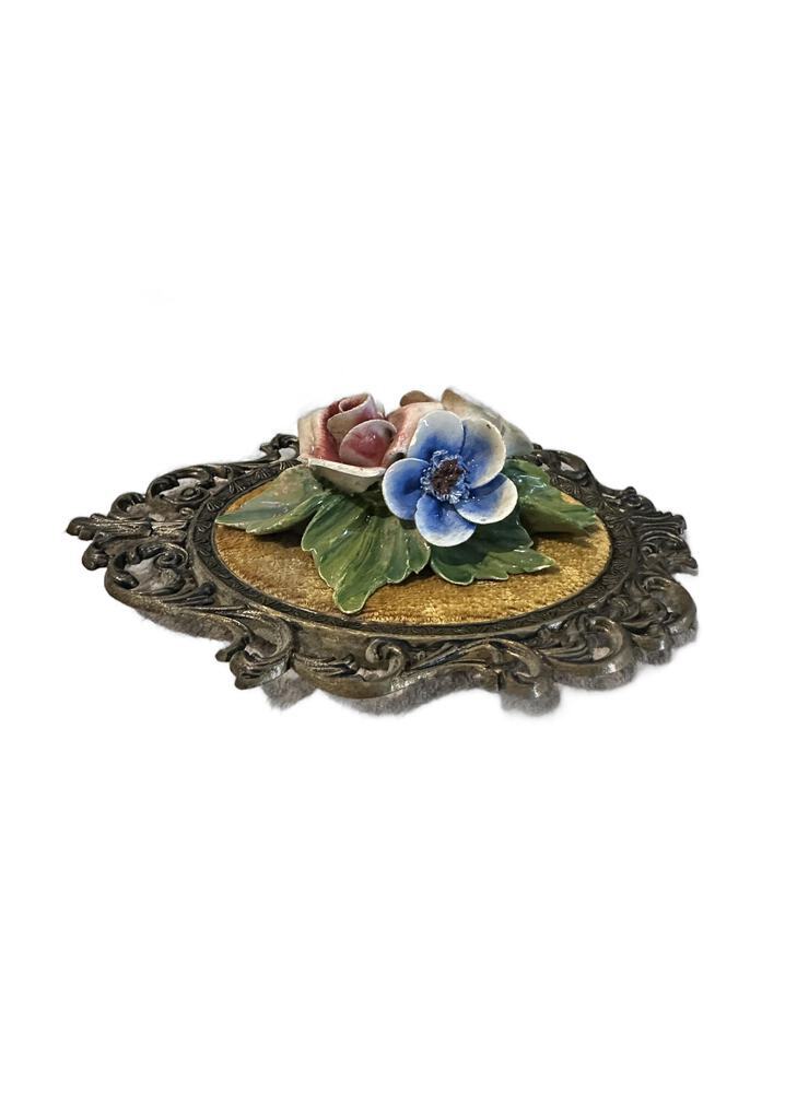 Angled view of pink rose and blue porcelain blossom with green leaves on gold velvet plaque
