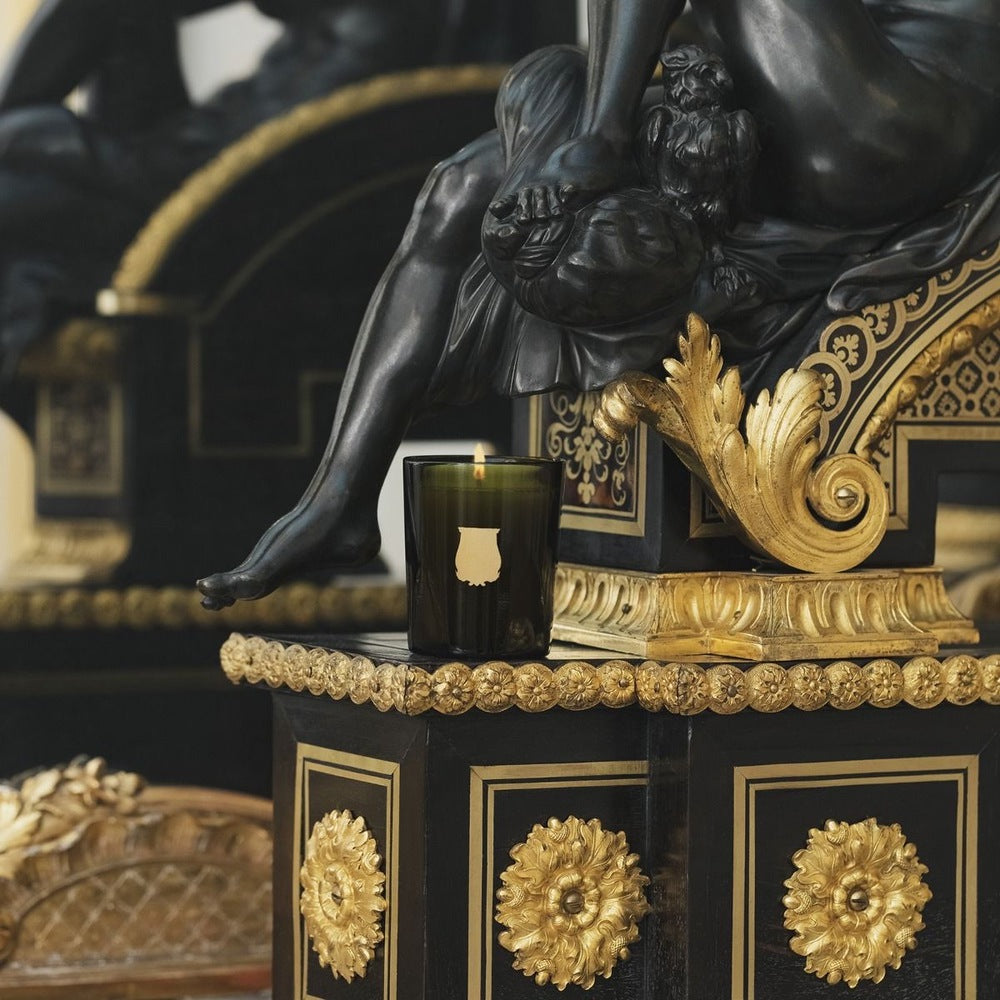 Green Trudon candle on a black-and-gilt pedestal beneath a dark bronze classical sculpture