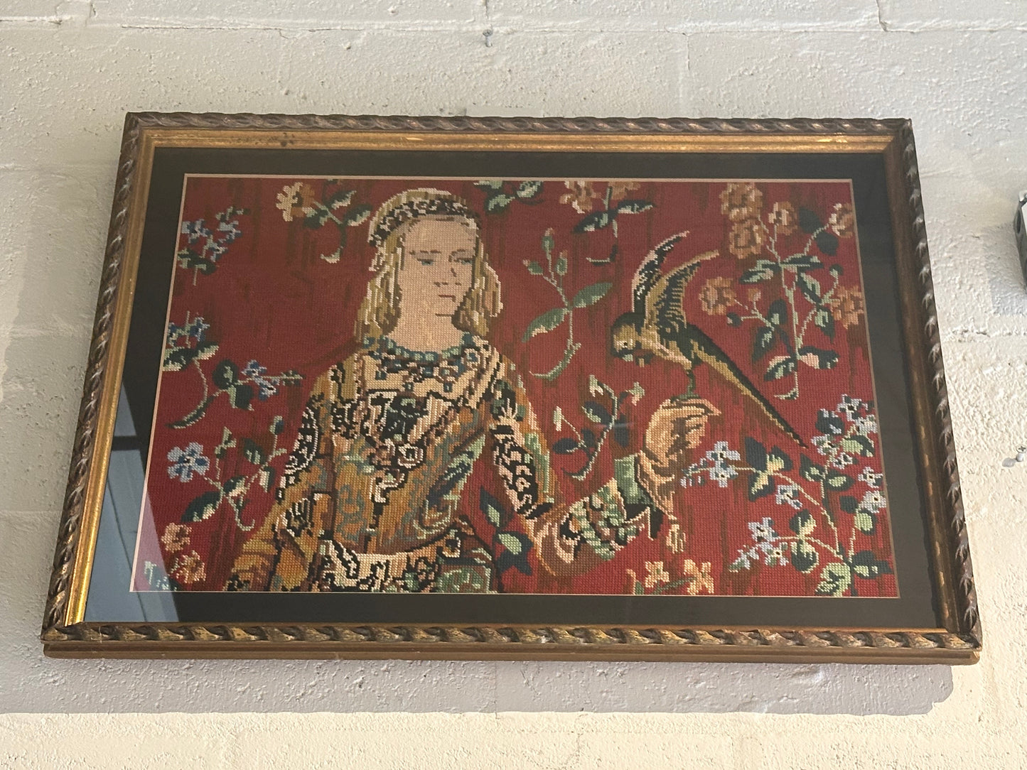 Restored framed needlepoint of a medieval lady and bird on red ground, hung on wall