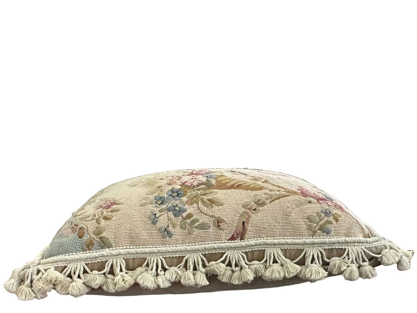 Side angle of needlepoint pillow showing floral motif and full cotton tassel fringe