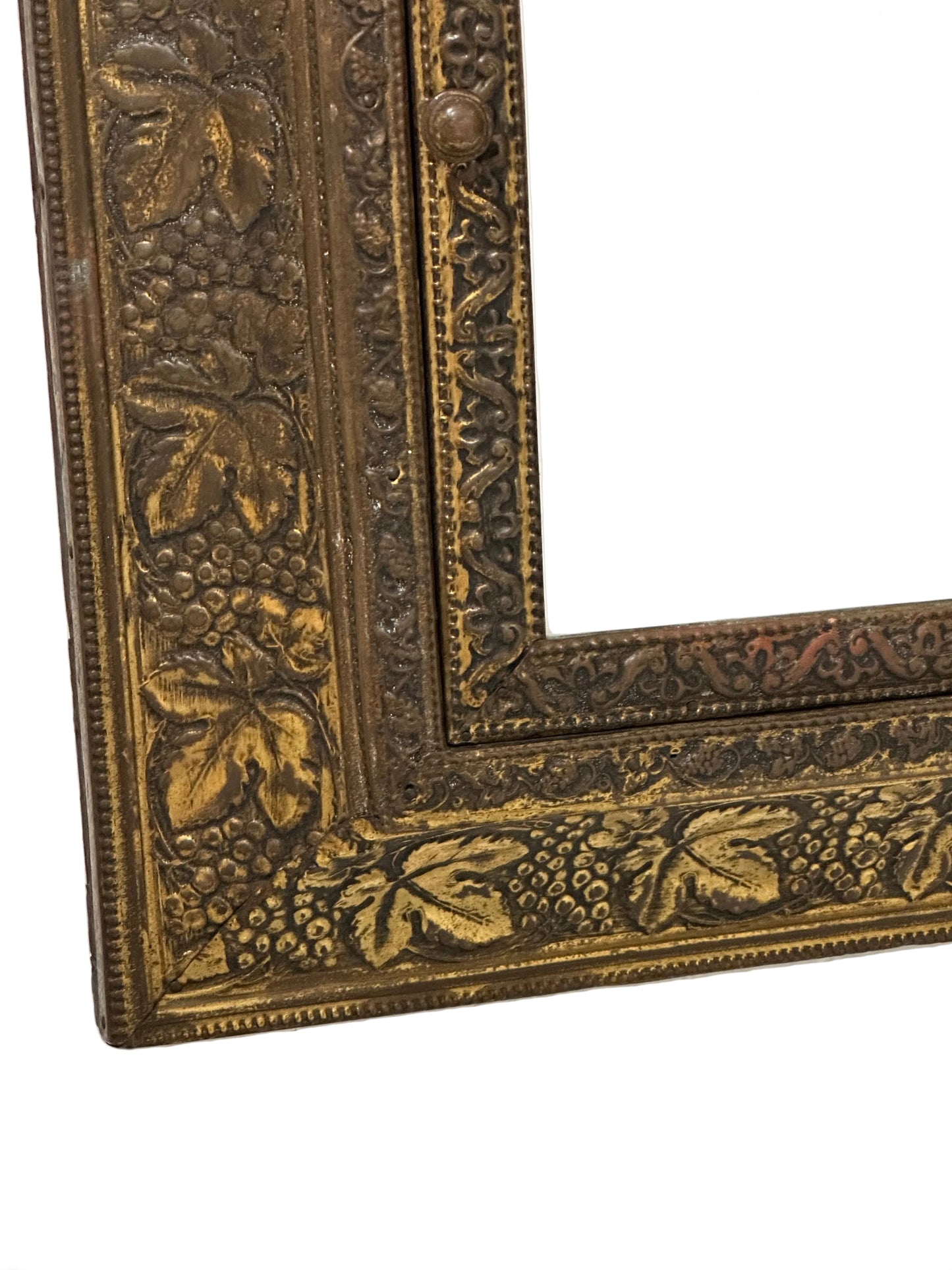 Lower corner detail of brass clothes-care cabinet showing grapevine repousse frame and bevel mirror.