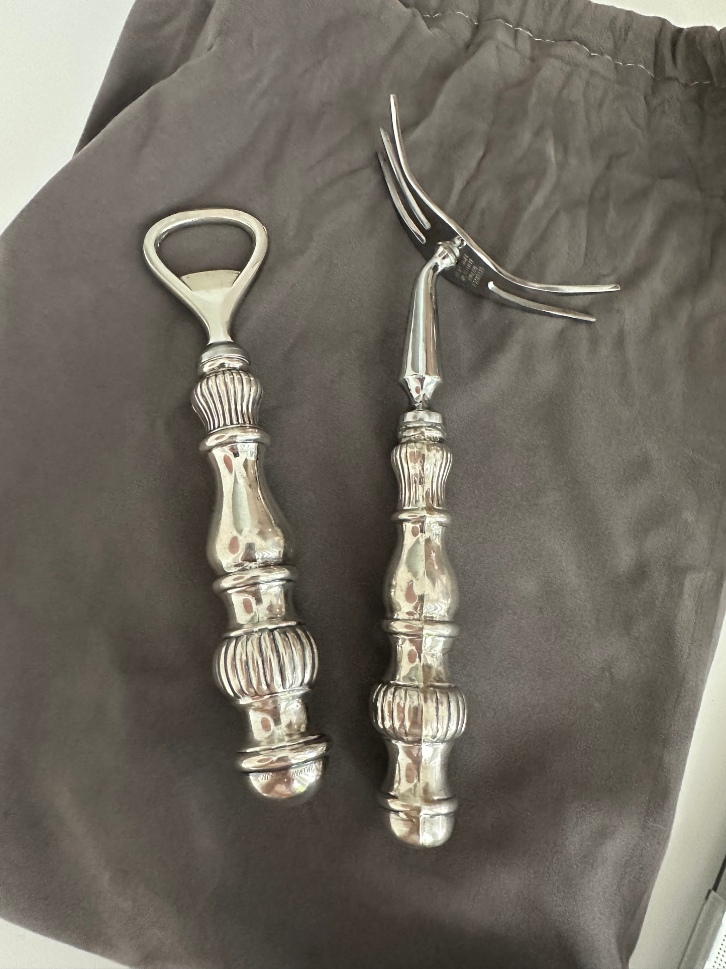 Vintage sterling fluted bar tools, bottle opener and cocktail fork laid on grey cloth.