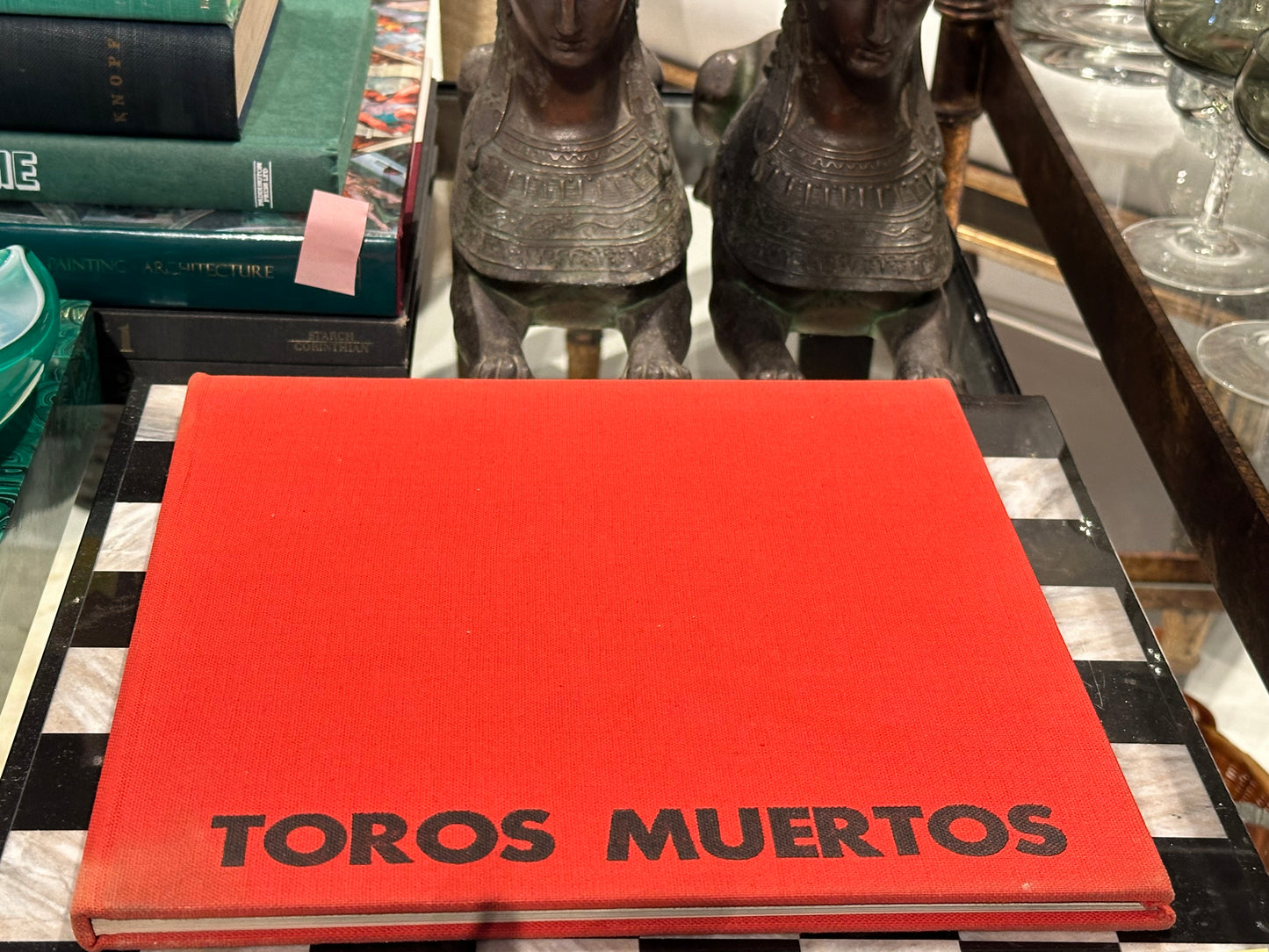 Vintage book Toros Muertos, red cloth cover displayed on tray beside bronze sphinx figures