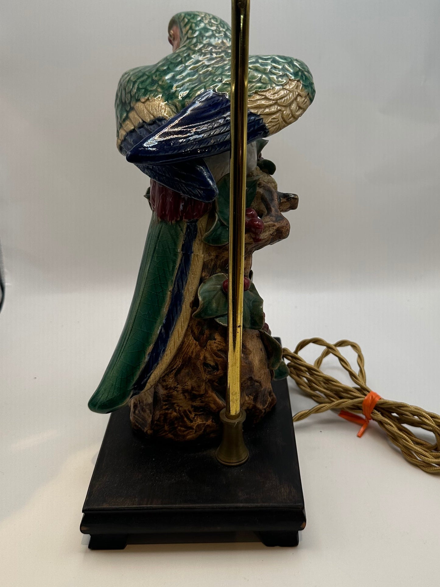 Side rear view of the parrot lamp showing the brass support rod, cord and wood stand