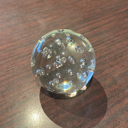 Clear bubble glass sphere paperweight with bubble pattern, side view on wood