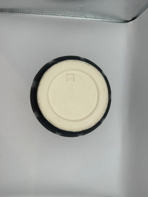 Underside of the black ceramic vessel showing cream foot ring and incised maker's mark