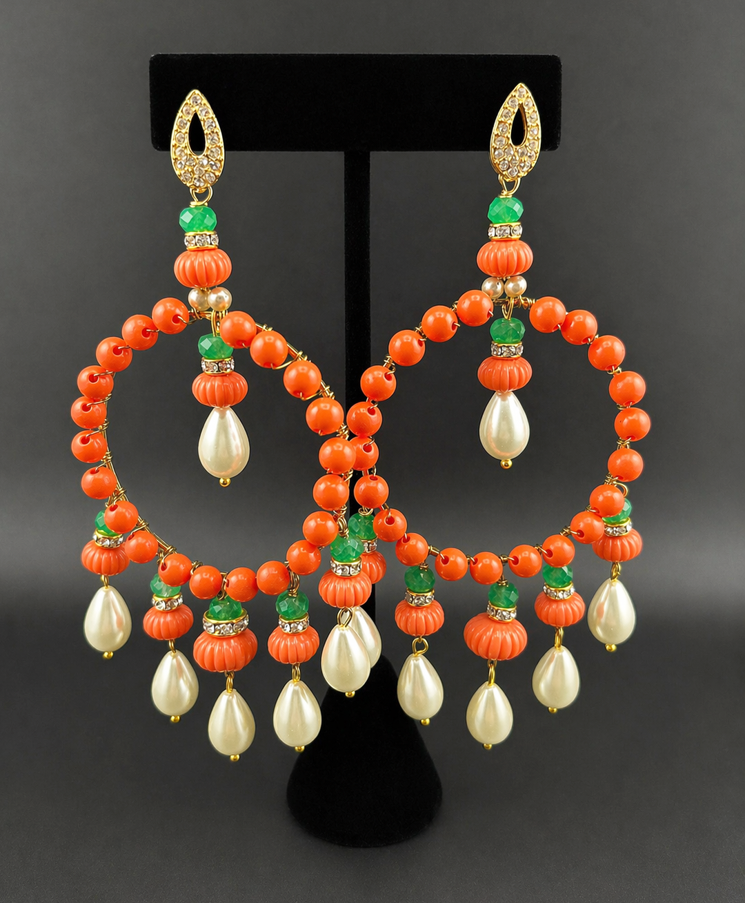 Coral hoop chandelier earrings displayed on black stand, orange beads, green stones, dangling pearls