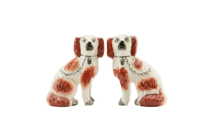 Pair of antique Staffordshire spaniel dog figurines, white with rust-red markings and gold chains, facing front.