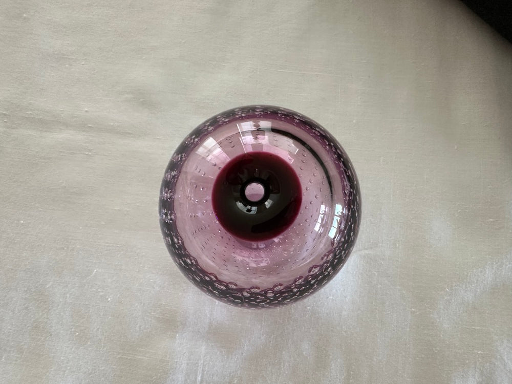 Top view of the amethyst Murano-style vase on linen, small bud opening at the center.