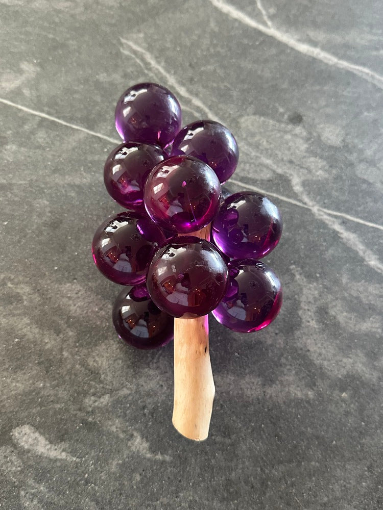 MCM purple acrylic grapes on a driftwood stem standing upright on gray stone