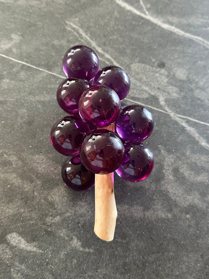 MCM purple acrylic grapes on a driftwood stem standing upright on gray stone