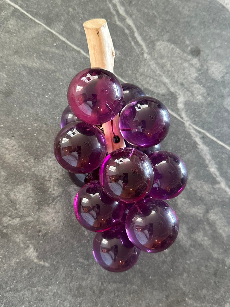 MCM purple acrylic grapes on a driftwood stem standing stem-up on gray stone
