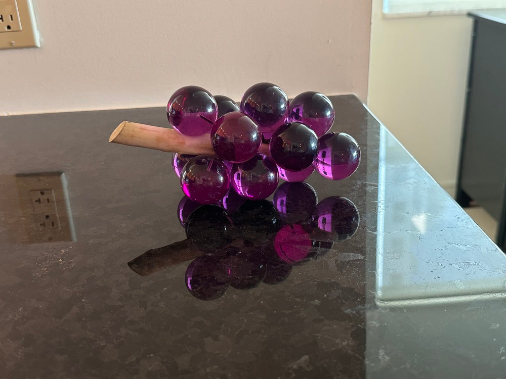 MCM purple acrylic grapes on a driftwood stem, side view with reflection on a dark counter