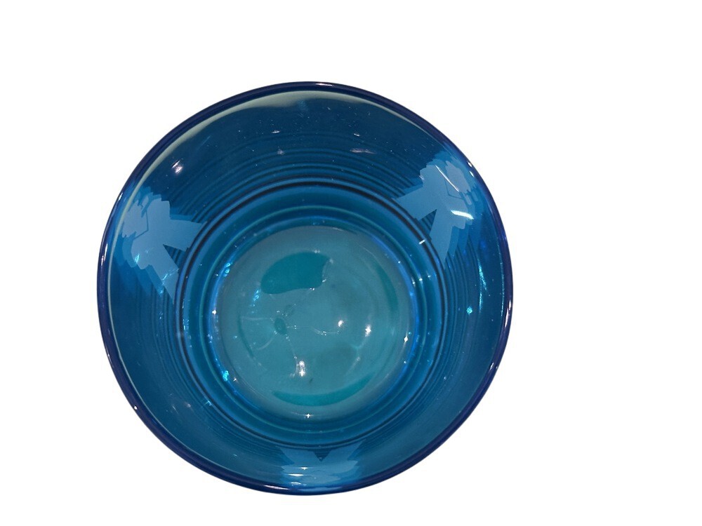 Top-down view into a blue rocks glass showing the base and sailor silhouettes through the glass.