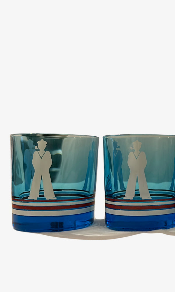Two blue sailor-motif rocks glasses close up, white sailor figure over red, white and blue stripes.