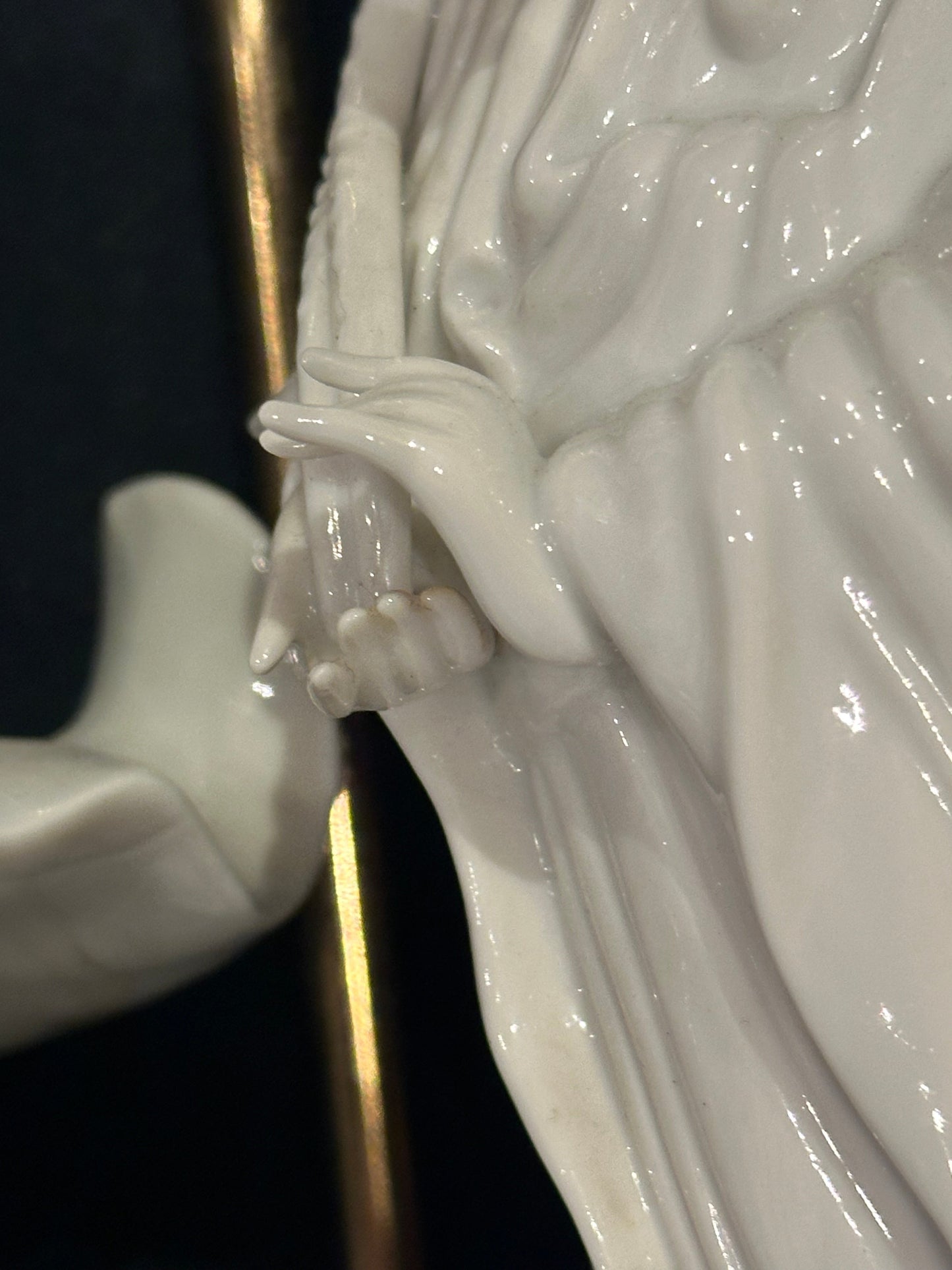 Close-up of a porcelain figure's hand and flowing robe beside the lamp's brass rod