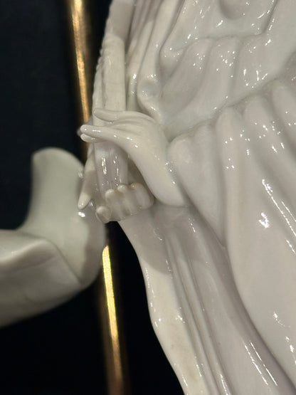 Close-up of a porcelain figure's hand and flowing robe beside the lamp's brass rod