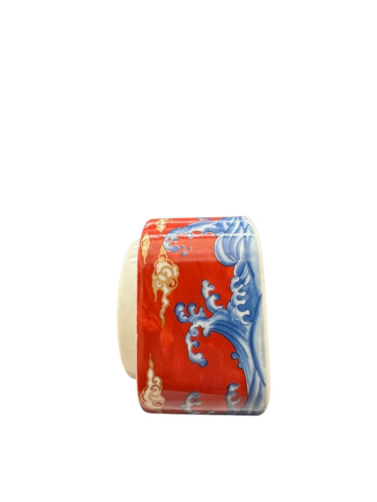 Vintage porcelain small box, angled side view showing blue wave decoration on red.