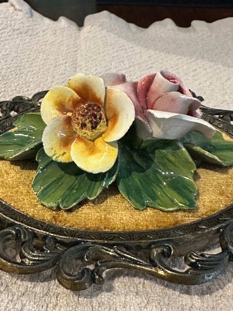 Close-up of porcelain yellow open flower and pink rose with green leaves on gold velvet
