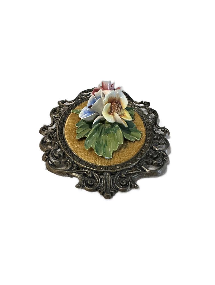 Overhead view of porcelain flower cluster, blue, yellow and pink blooms, on gold velvet plaque