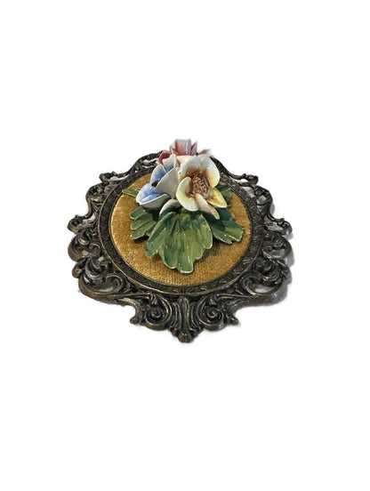 Overhead view of porcelain flower cluster, blue, yellow and pink blooms, on gold velvet plaque