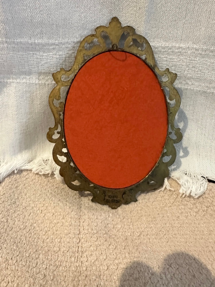 Back of floral plaque showing orange-red velvet backing and pierced metal frame on fabric surface
