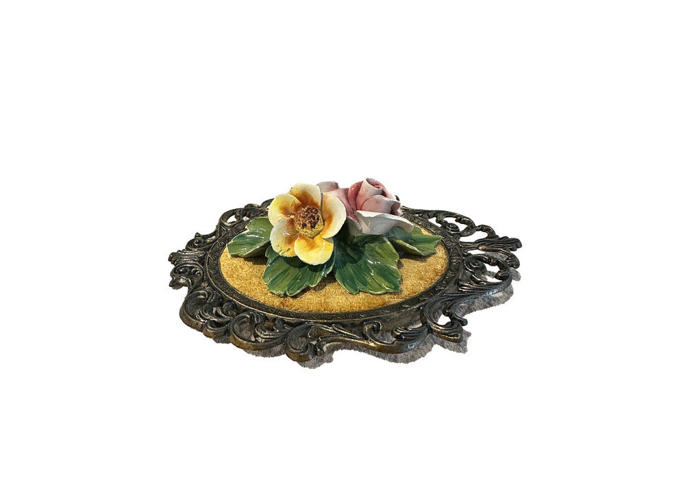 Side angled view of raised porcelain flowers and leaves on gold velvet plaque in dark scrolled frame