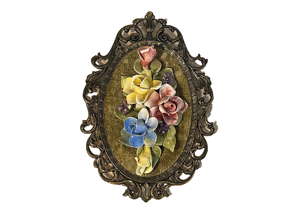 Angled front view of Capodimonte porcelain floral plaque, pink, yellow and blue roses on green velvet in scrolled gilt frame
