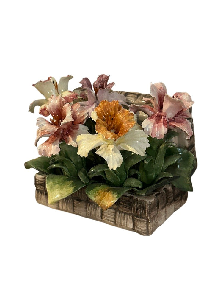 Capodimonte porcelain flowers in a woven-basket base, angled front view with green leaves