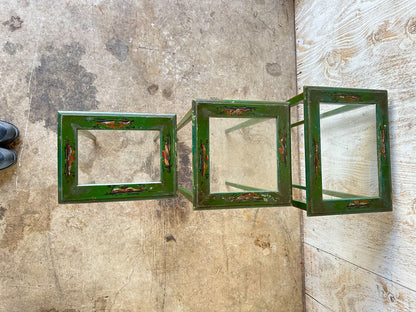 Three green lacquered nesting tables laid flat side by side, worn painted decoration