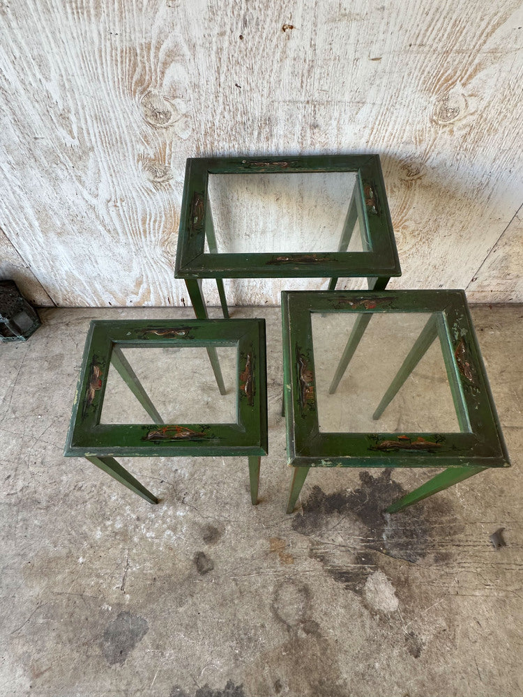 Angled view of three green lacquered nesting tables with glass tops and tapered legs