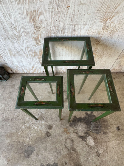 Angled view of three green lacquered nesting tables with glass tops and tapered legs