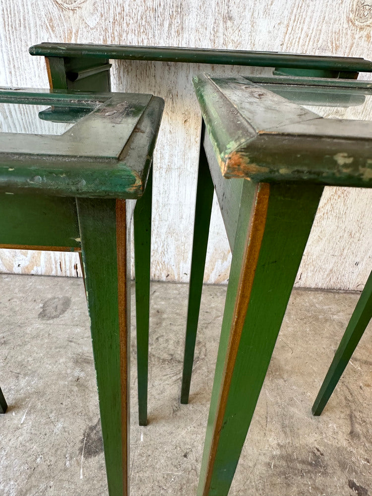 Close-up of green lacquered nesting table legs and tops against weathered wood backdrop