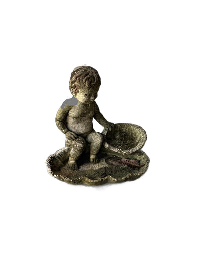 Vintage weathered concrete cherub seated beside a shell basin on a leaf-shaped base, mossy patina