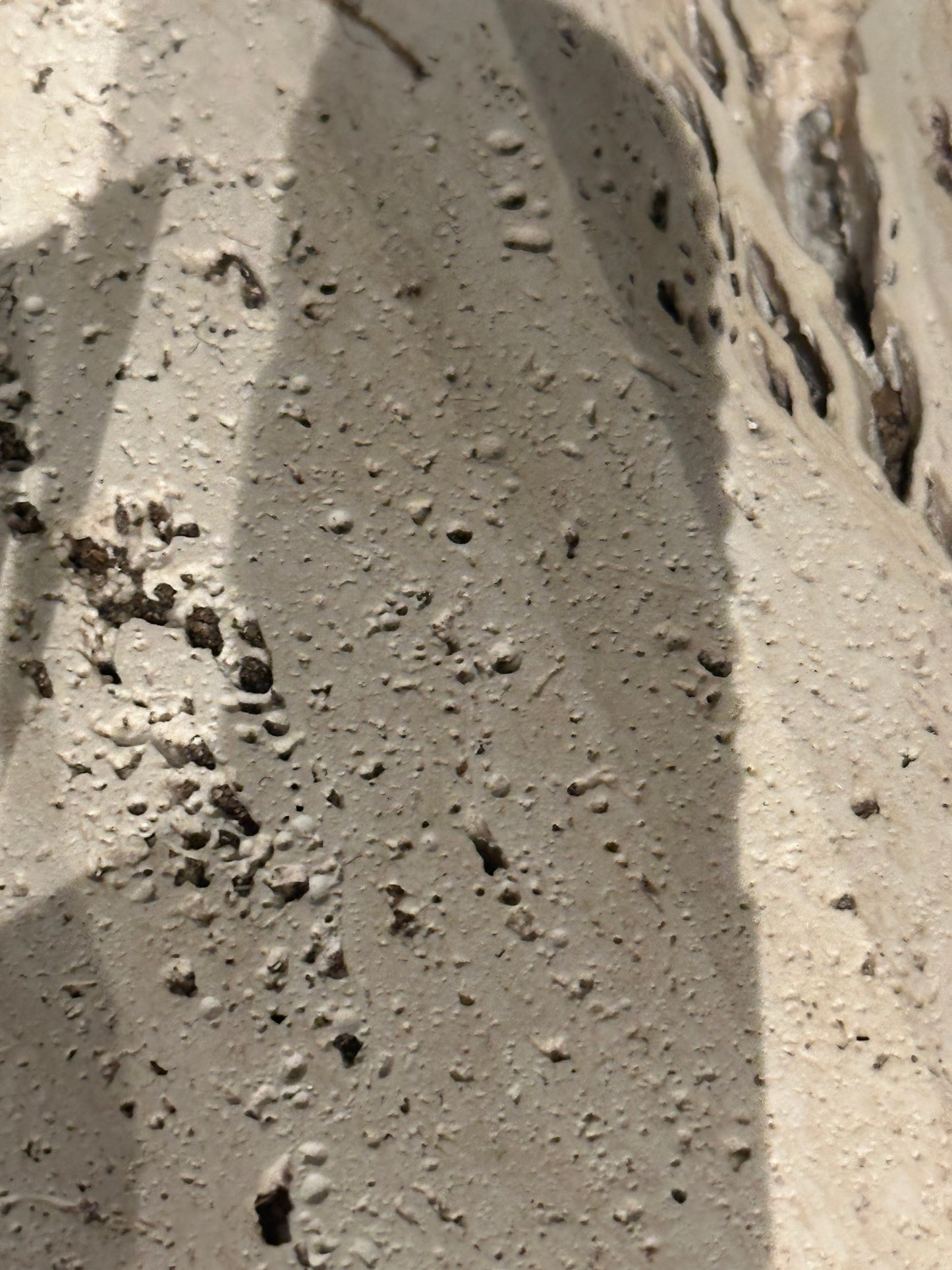 Close-up of the porous, pitted travertine surface of a limestone pedestal.