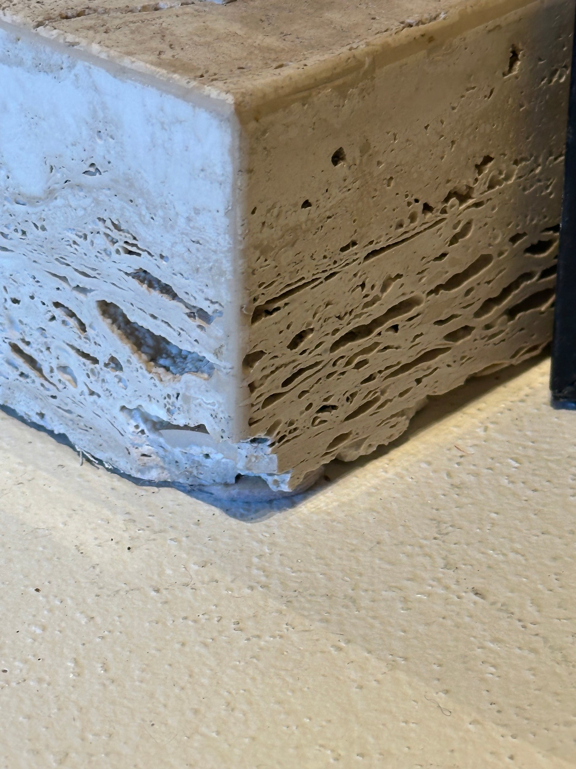 Close-up of the pitted travertine base corner of a limestone pedestal showing minor chips.