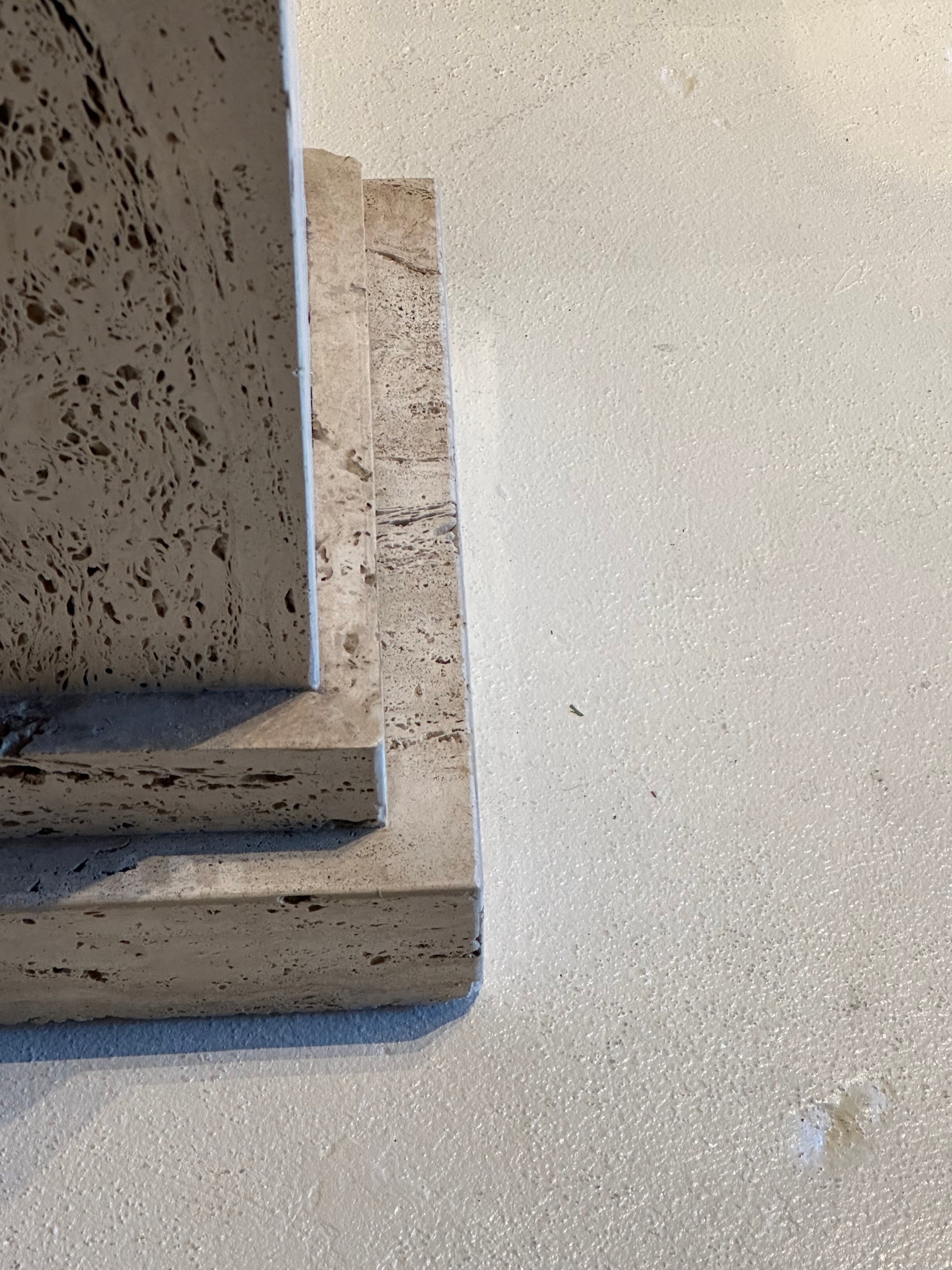 Close-up of the stepped base and pitted travertine surface of a limestone pedestal.