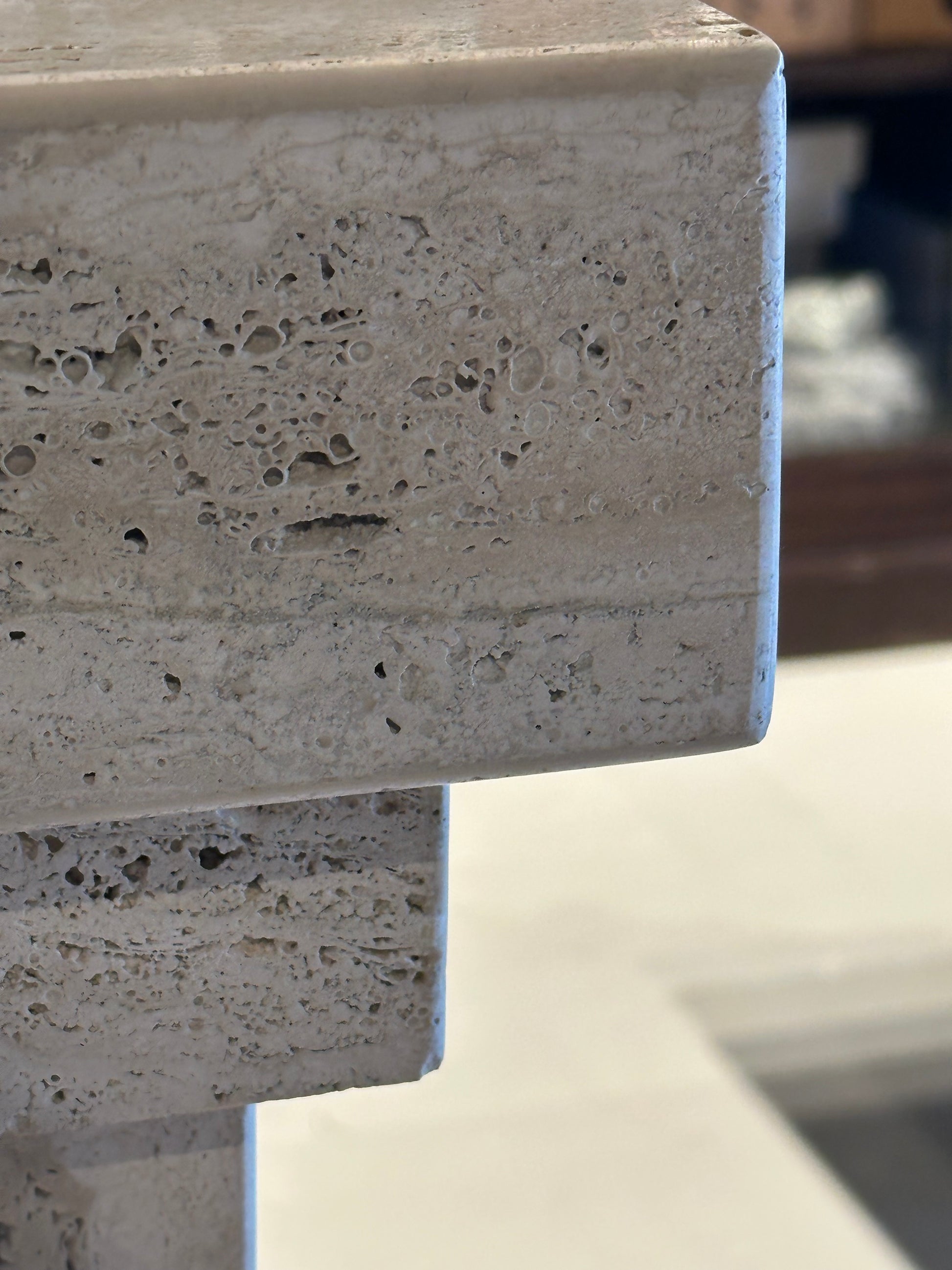 Close-up of the square top edge and porous travertine texture of the pedestal.