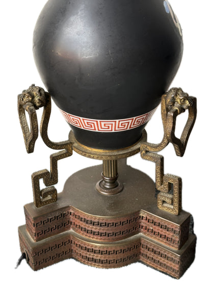 Close-up of a black lamp's base, red Greek-key band, gilt-bronze lion-head handles and stepped plinth