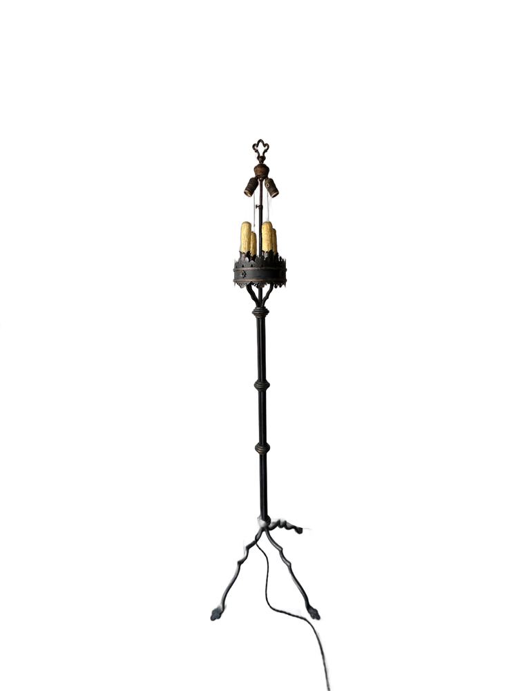 Iron floor lamp at full length, slender shaft rising from arched tripod feet to the candle cluster