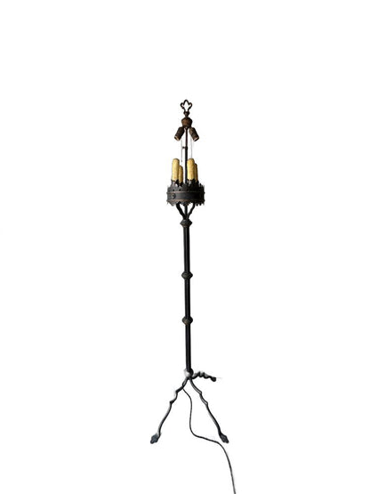 Iron floor lamp at full length, slender shaft rising from arched tripod feet to the candle cluster