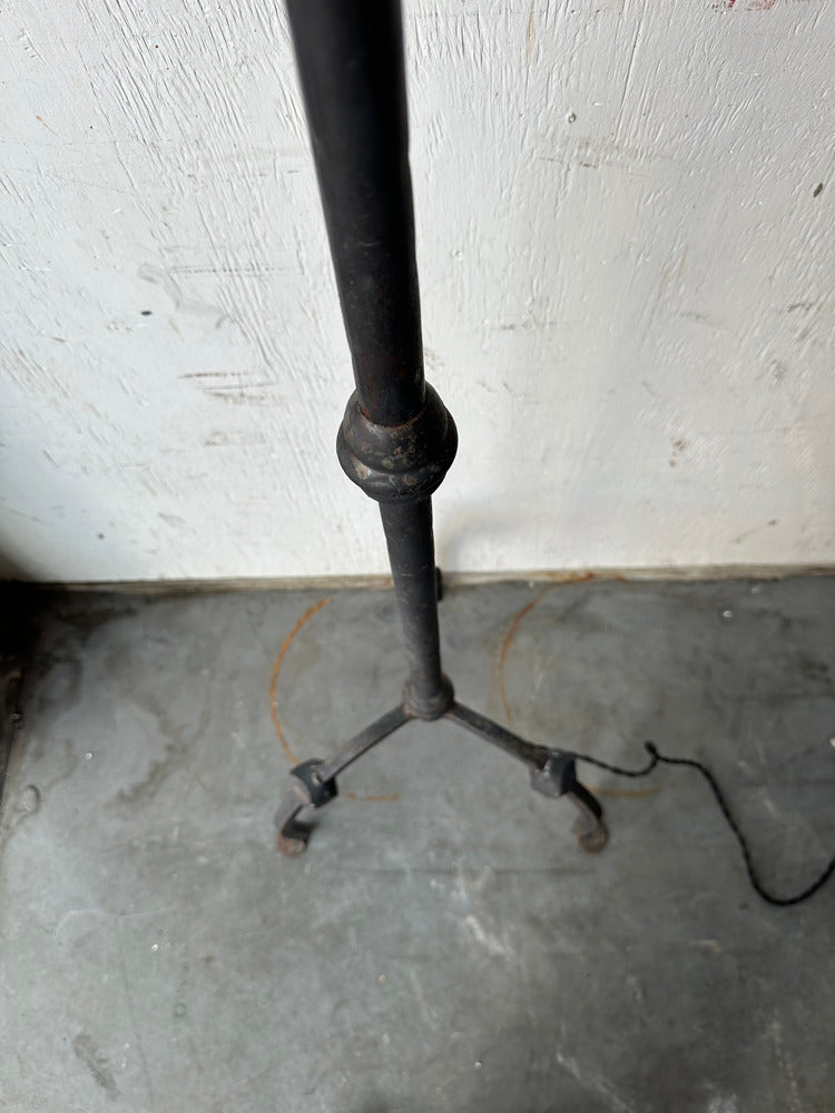 Vintage iron floor lamp's tripod base with scrolled feet, shown on concrete floor