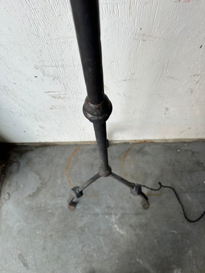 Vintage iron floor lamp's tripod base with scrolled feet, shown on concrete floor