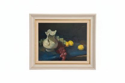 Vintage still life painting, cream pitcher with grapes and lemons on dark table, limed wood frame