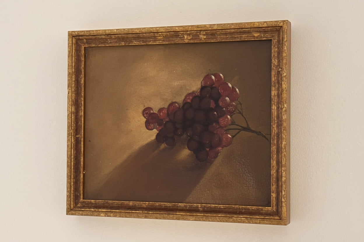 Framed grapes still life oil painting, angled view of gilt wood frame against pale wall