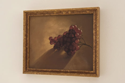 Framed grapes still life oil painting, angled view of gilt wood frame against pale wall