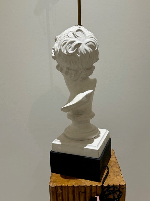 Plaster bust lamp on black plinth atop a wood pedestal, shown beside a wall