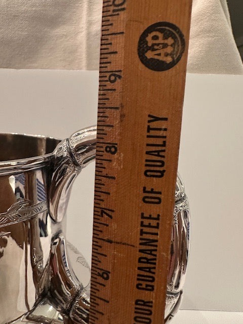Silver pitcher beside a wooden ruler measuring its height at roughly 8 inches
