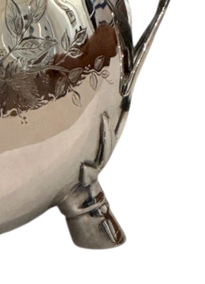 Close-up of the silver pitcher's leaf-form foot and engraved floral body detail
