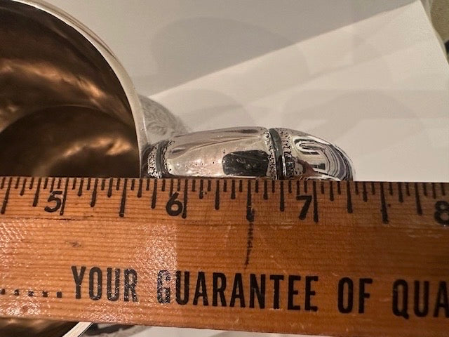 Silver pitcher rim and handle beside a ruler measuring across 5 to 7 inches